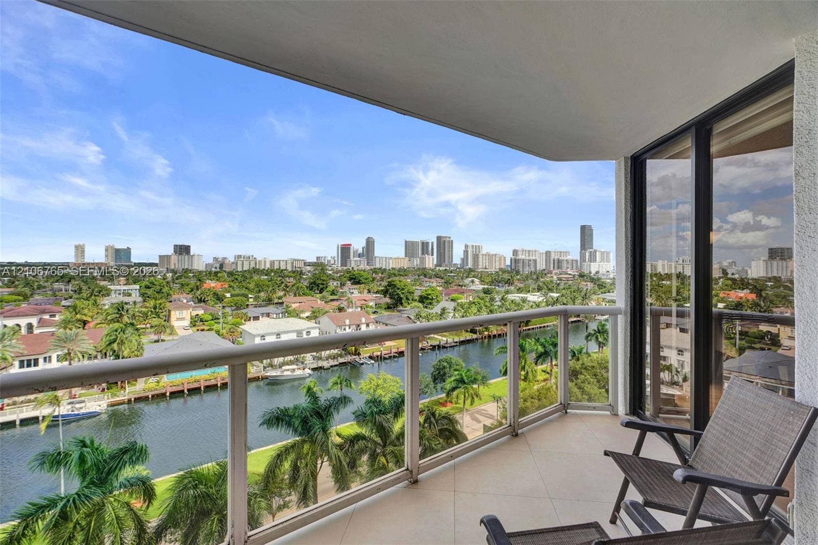 3598 Yacht Club Drive, #901, Aventura, FL 33180 Covered balcony overlooking a canal, tropical landscaping, and a distant city skyline.