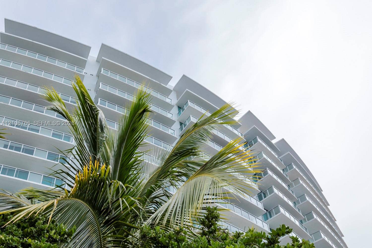 Modern multi-story facade featuring stepped exterior balconies, full-height glass sliders, and sleek white structural overhangs