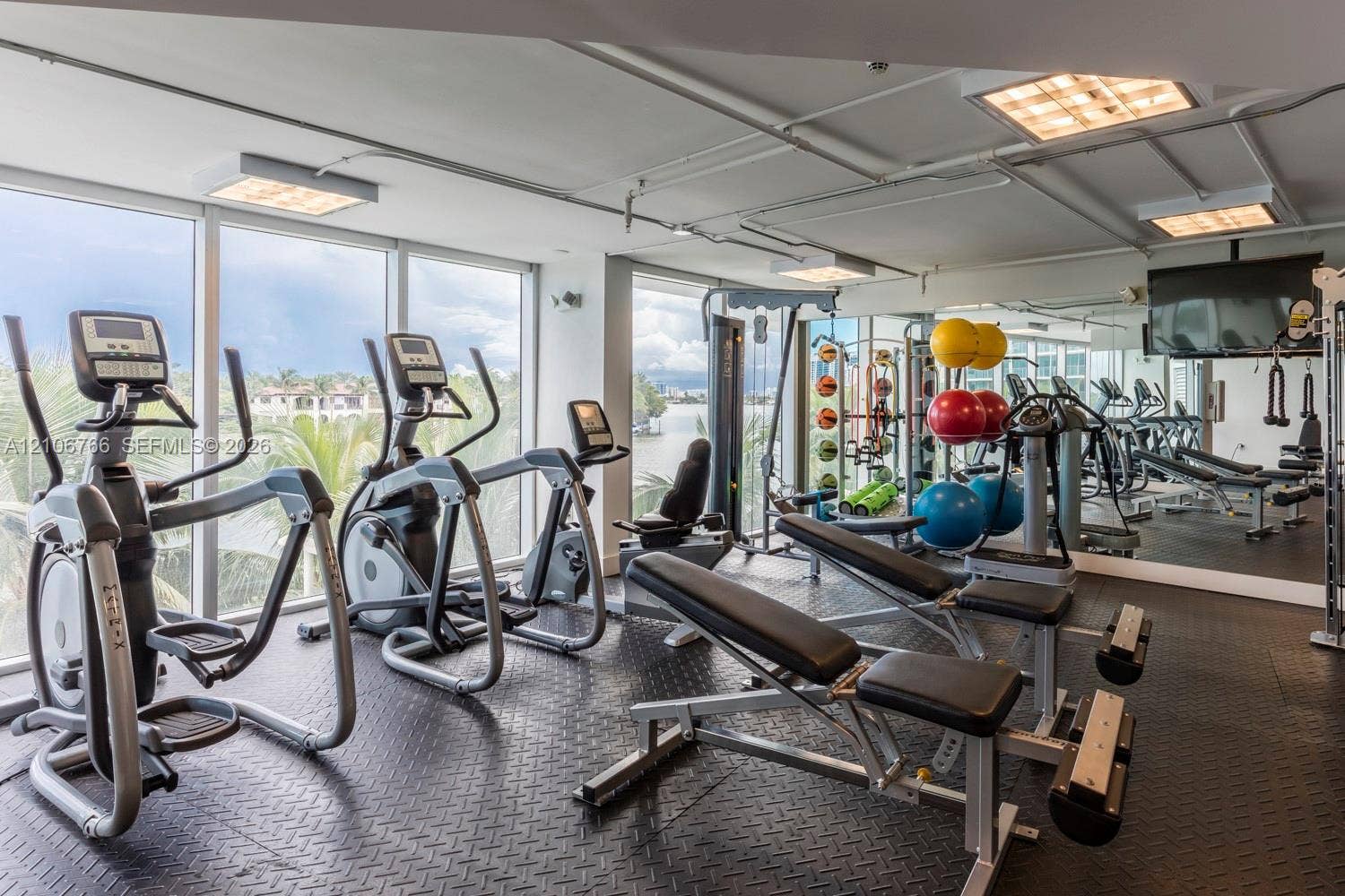 Fitness center featuring floor-to-ceiling windows, mirrored walls, textured rubber flooring, and exposed ceiling lighting
