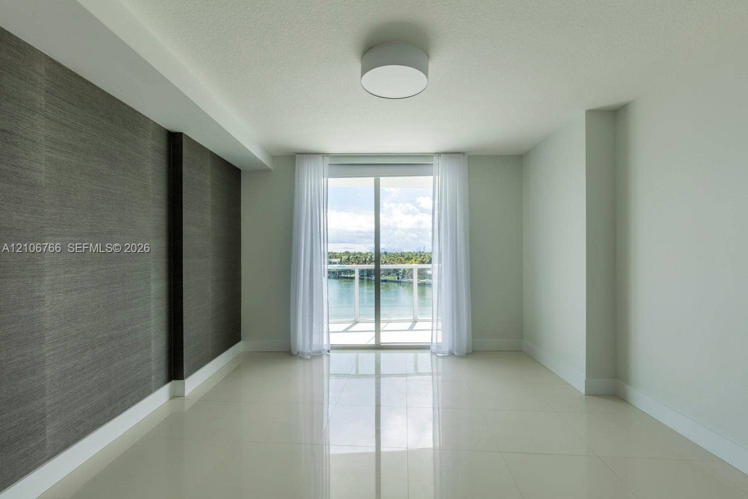 Interior space featuring large-format tile flooring, textured charcoal accent wall, flush-mount ceiling lighting, and sliding glass doors leading to a balcony