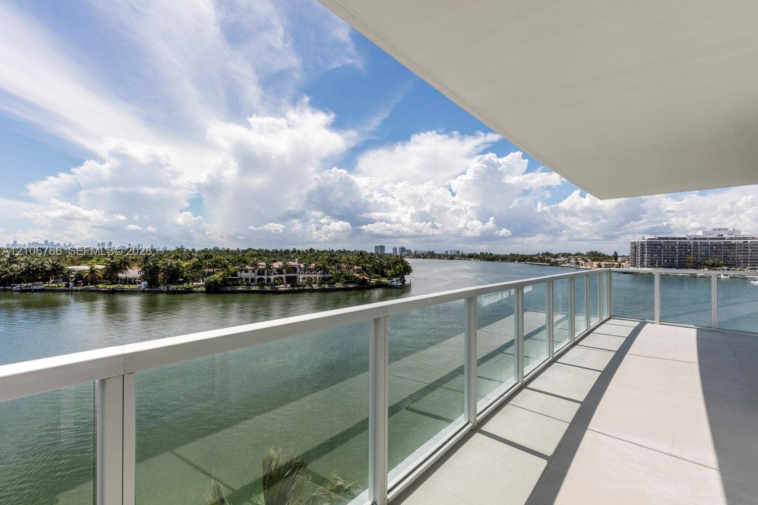 Expansive balcony featuring a glass panel railing, concrete flooring, and an overhead canopy