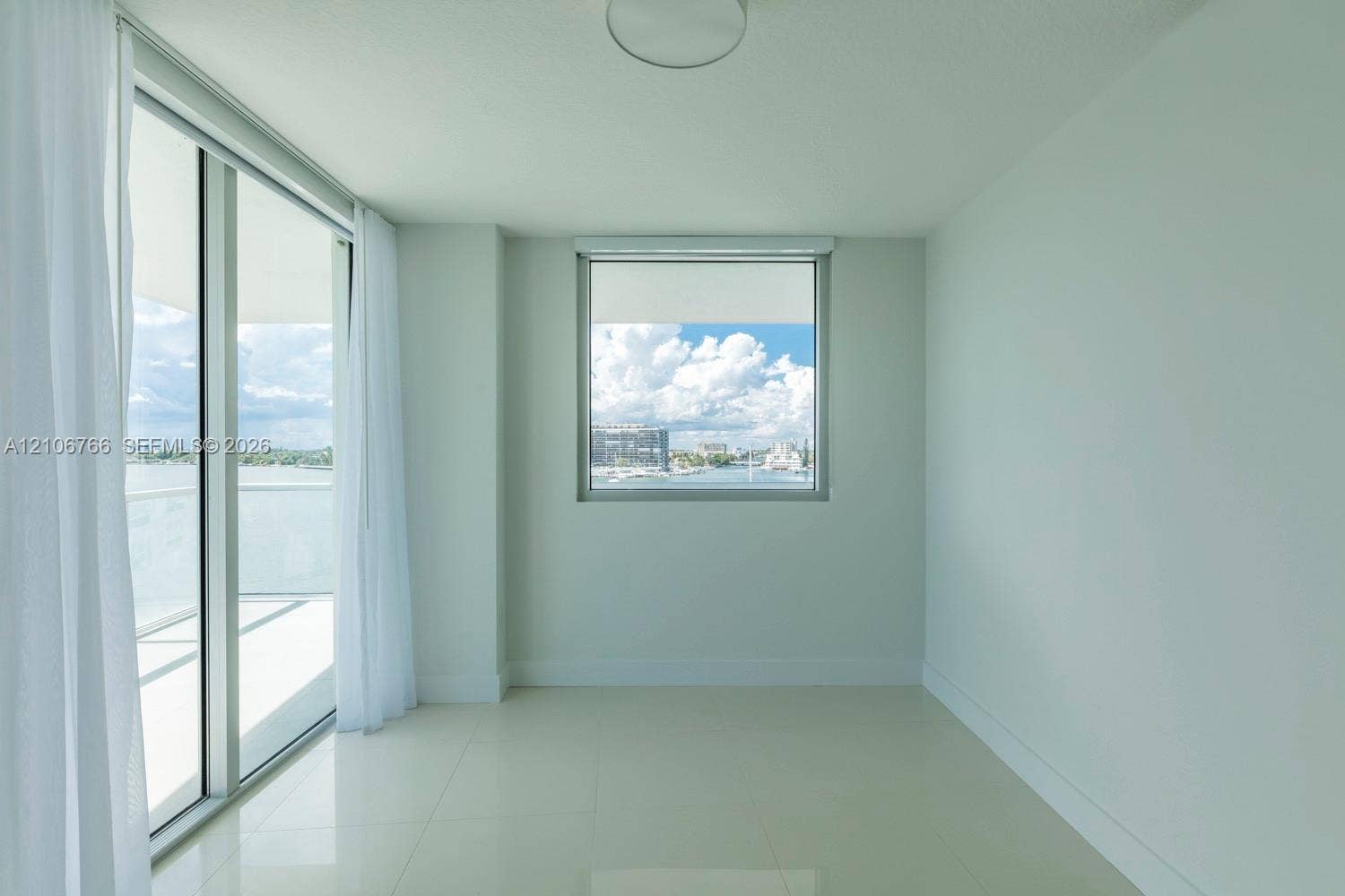 Floor-to-ceiling sliding glass doors, polished tile flooring, neutral wall finish, and energy-efficient windows with water scenery