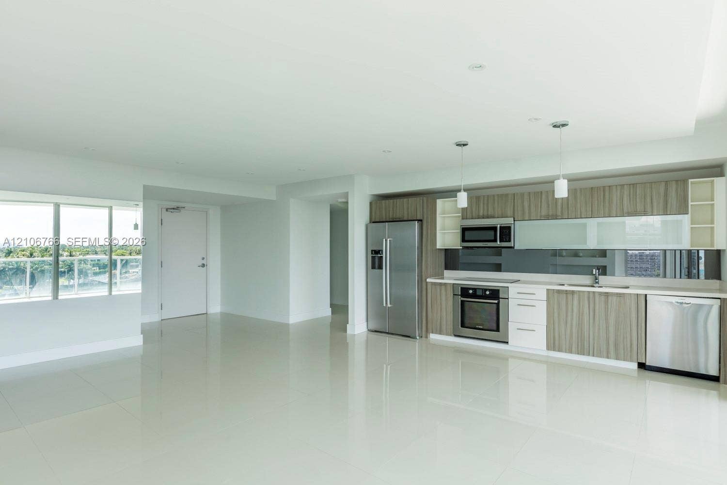 Open-concept area featuring polished tile flooring, wood-finish cabinetry, stainless steel appliances, glass-panel upper cabinet doors, and integrated pendant lighting