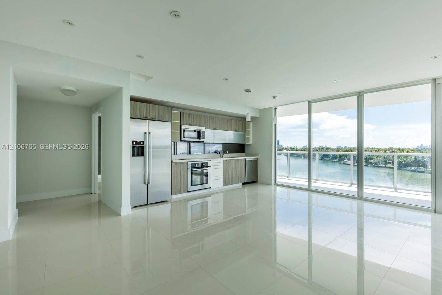 Open-concept interior featuring light-toned tile flooring, recessed ceiling lighting, stainless steel appliances, horizontally-grained cabinetry, and floor-to-ceiling glass panel doors