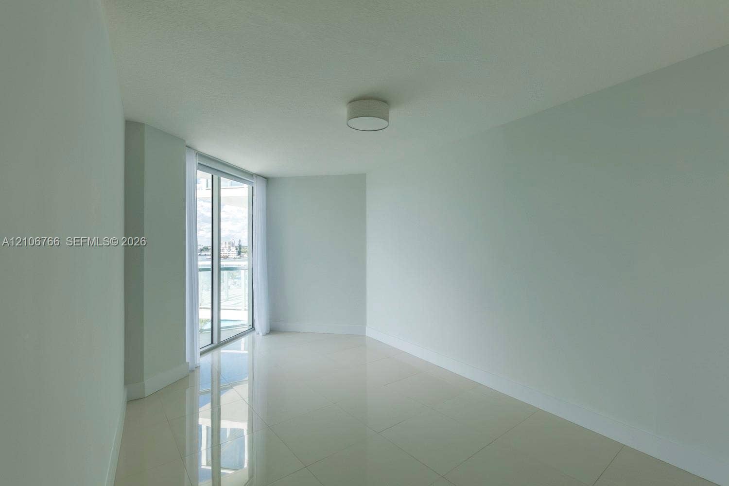 Expansive room featuring neutral wall tones, large-format tile flooring, a minimalist ceiling-mounted light fixture, and floor-to-ceiling glass sliding doors