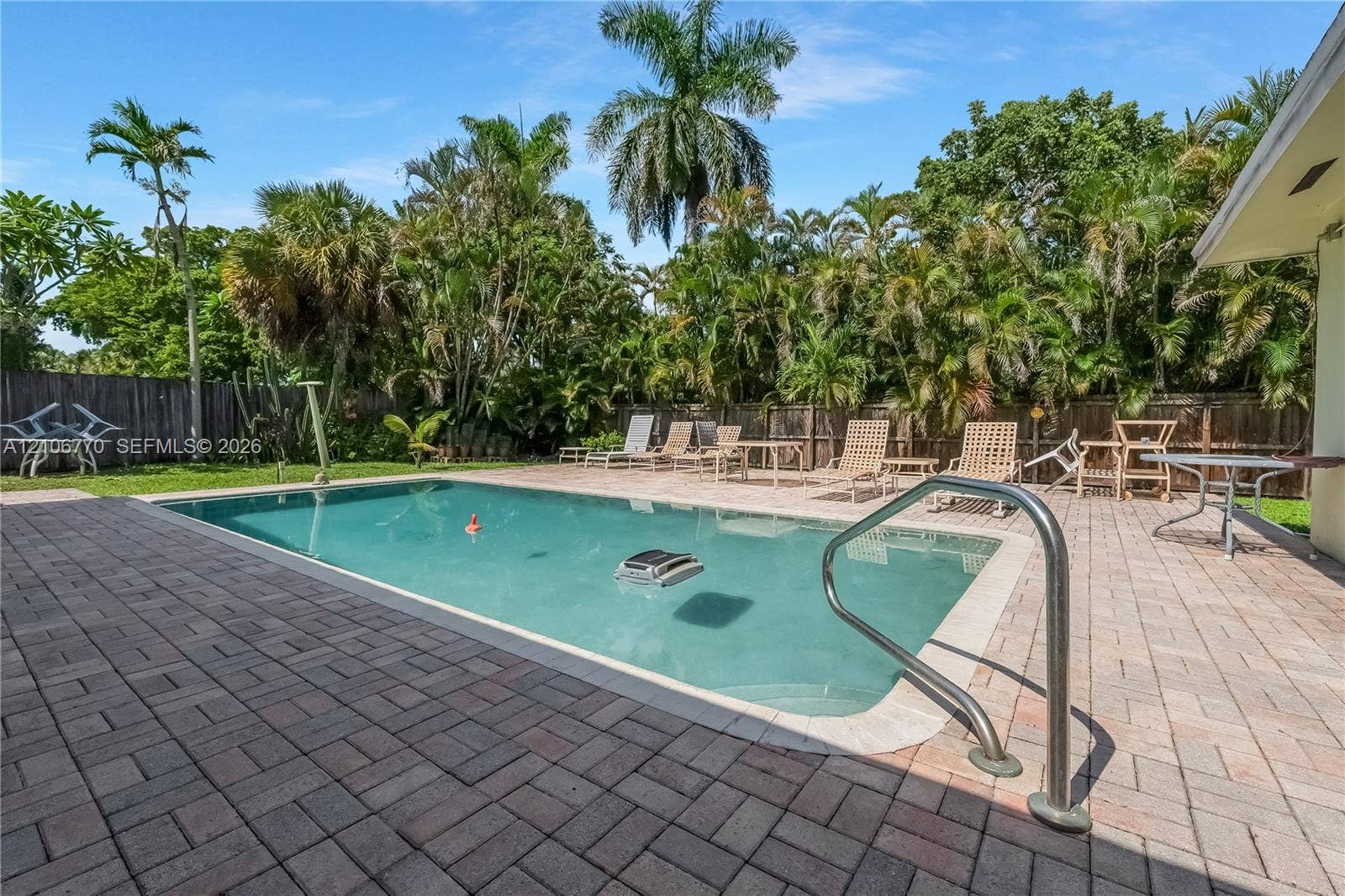 5701 SW 1st Street, Plantation, FL 33317 In-ground swimming pool with a metal handrail, surrounded by a paved stone patio, enclosed by a wood privacy fence and mature palm trees