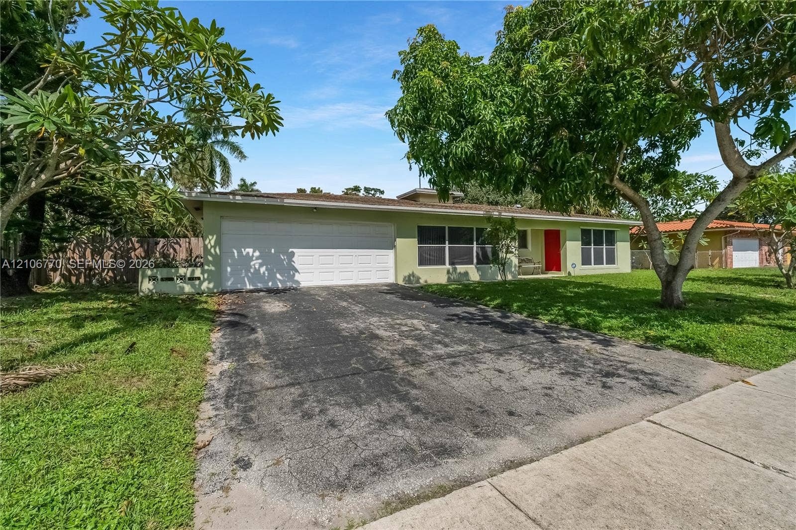 5701 SW 1st Street, Plantation, FL 33317 Single-story residence featuring a two-car garage, low-pitch roofline, and bright red front entry door set within a landscaped lot with mature trees