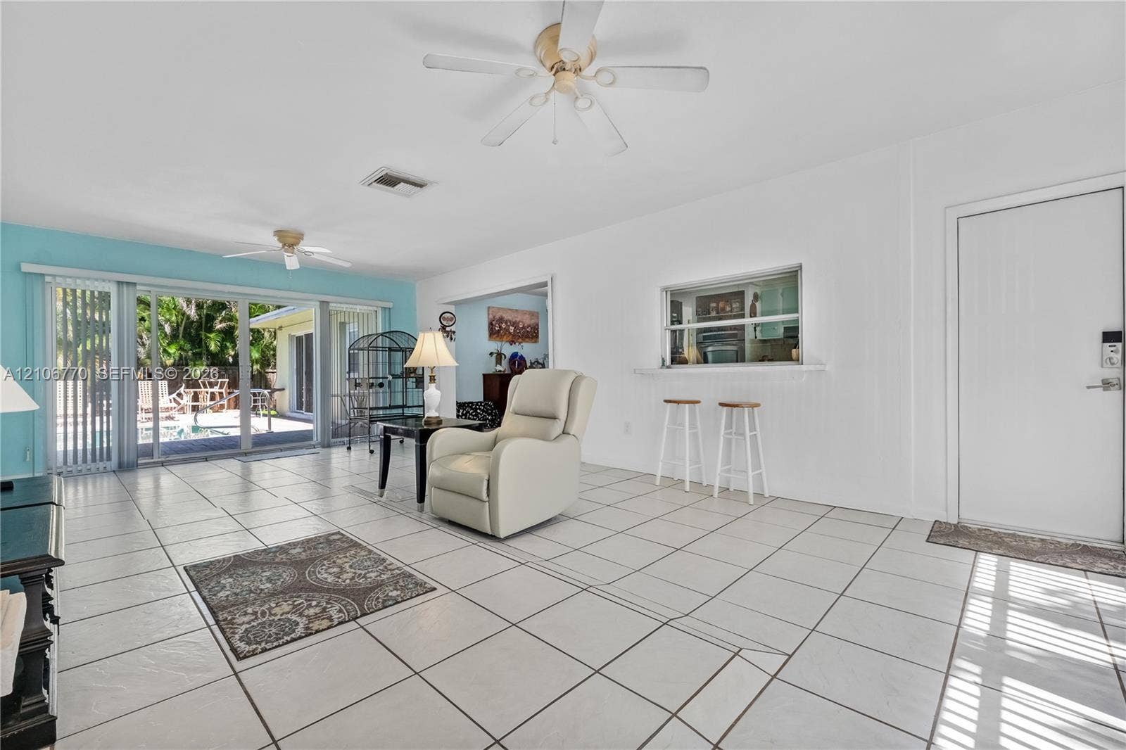 5701 SW 1st Street, Plantation, FL 33317 Open-concept space featuring large-format tile flooring, dual ceiling fans, a pass-through service window, and floor-to-ceiling sliding glass doors