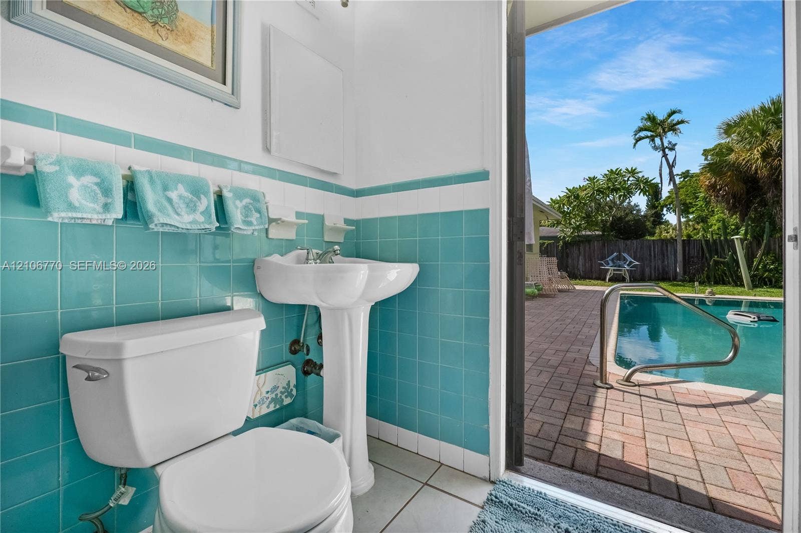 5701 SW 1st Street, Plantation, FL 33317 Ceramic tile wainscoting, white porcelain pedestal sink, and direct egress to a brick-paved pool deck