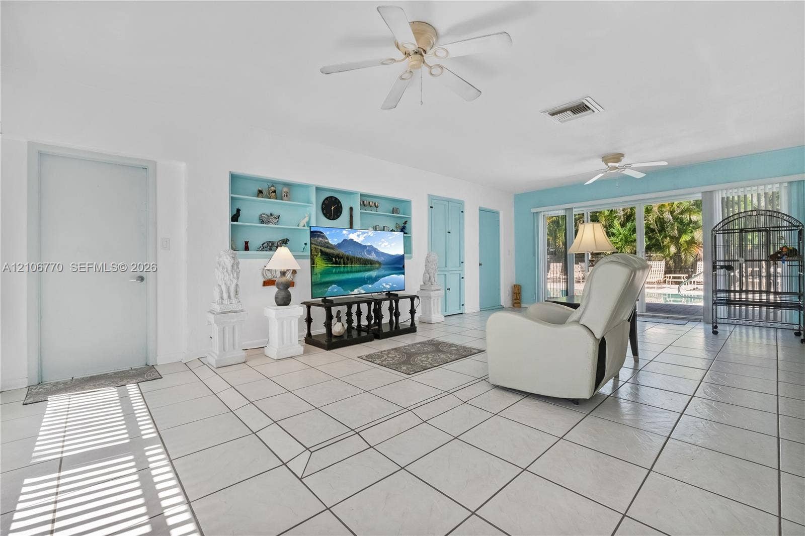 5701 SW 1st Street, Plantation, FL 33317 Living area featuring large-format tile flooring, built-in recessed shelving, dual ceiling fans, and a sliding glass door