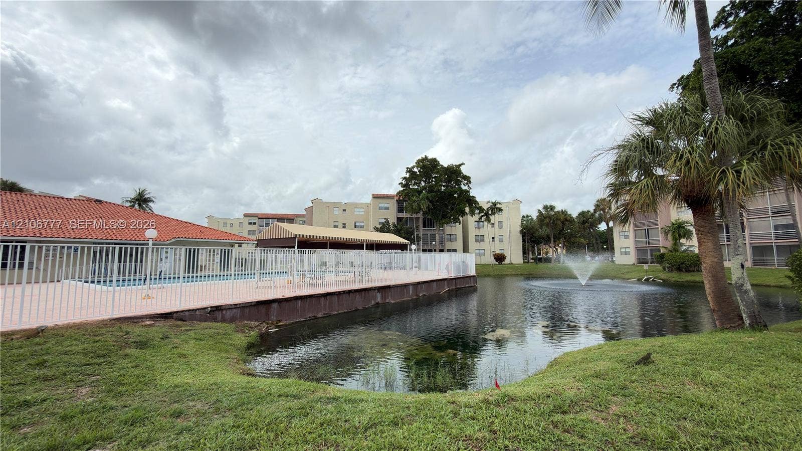 1810 SW 81st Avenue, #2200, North Lauderdale, North Lauderdale, FL 33068 Community pool featuring a terra-cotta tile roof, paved deck, protective perimeter fencing, and a waterfront location with an integrated fountain