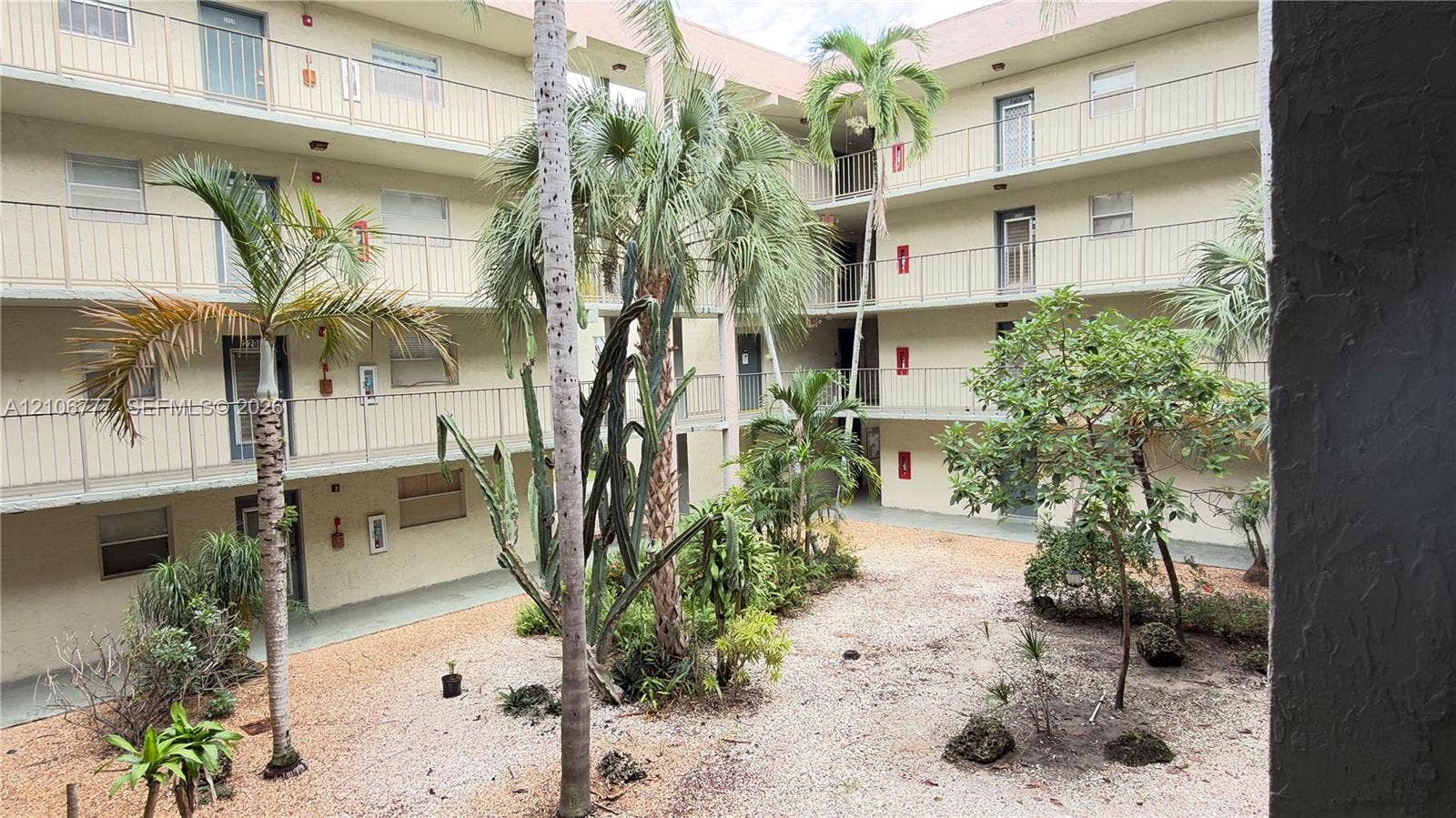 1810 SW 81st Avenue, #2200, North Lauderdale, North Lauderdale, FL 33068 Multi-story building exterior featuring open-air walkways, metal balcony railings, decorative palm trees, and landscaped ground-level garden