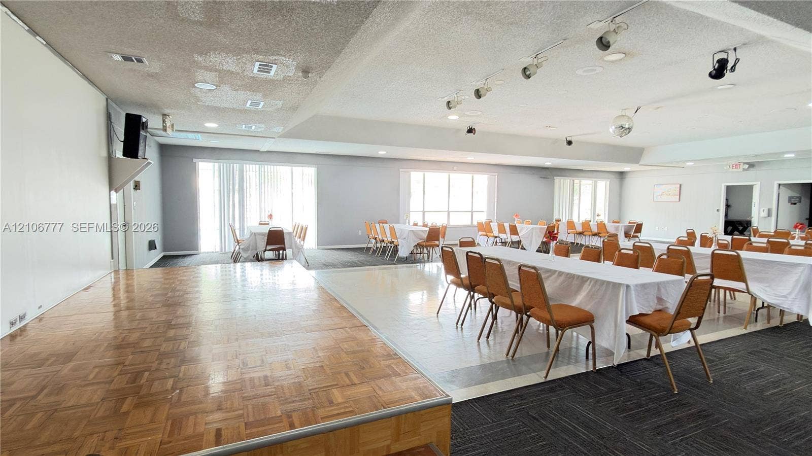 1810 SW 81st Avenue, #2200, North Lauderdale, North Lauderdale, FL 33068 Expansive open-concept interior featuring a raised wood-parquetry platform stage, multi-section track lighting, large windows with vertical blinds, and a combination of tile and carpeted flooring
