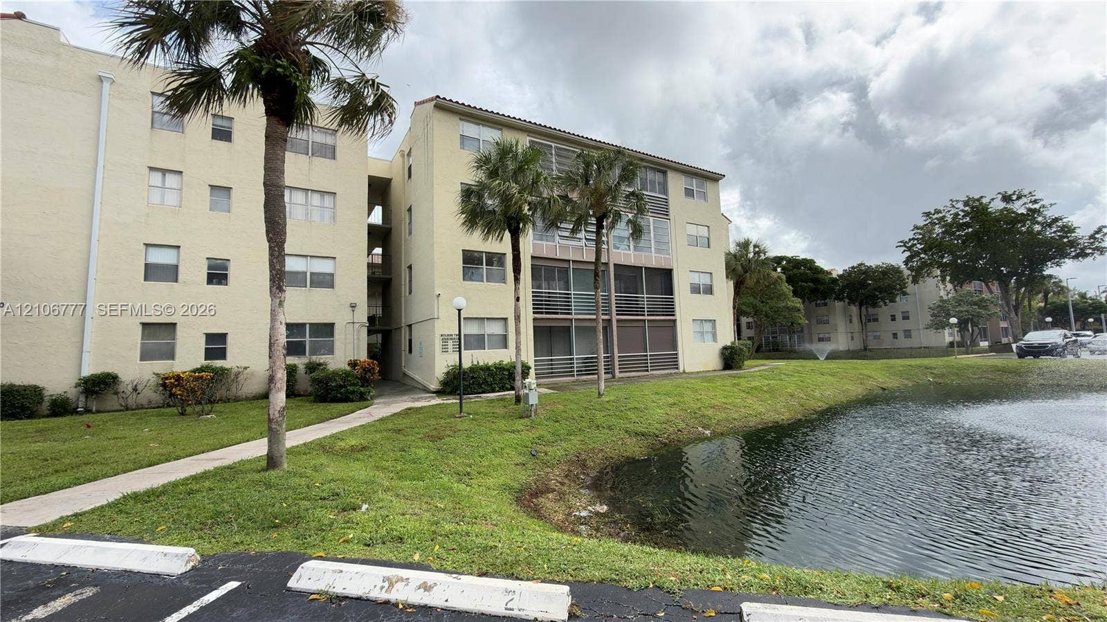 1810 SW 81st Avenue, #2200, North Lauderdale, North Lauderdale, FL 33068 Multi-story building exterior featuring stucco siding, screened balconies, concrete walkways, and mature palm trees situated on a waterfront lot