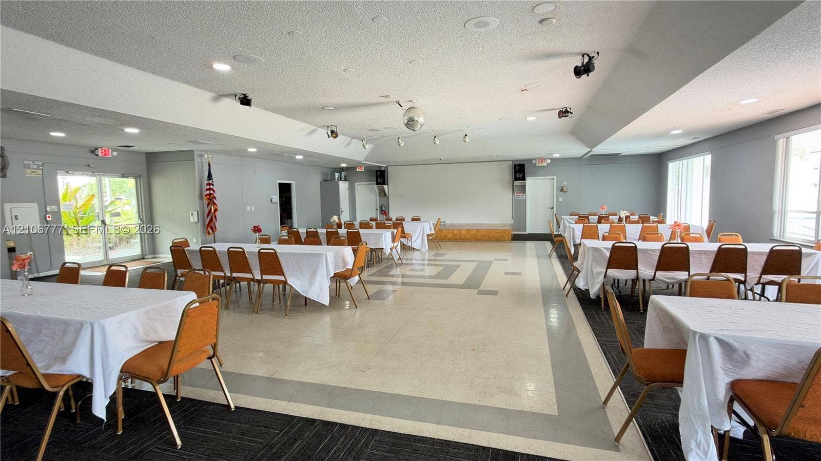 1810 SW 81st Avenue, #2200, North Lauderdale, North Lauderdale, FL 33068 Expansive multi-purpose hall featuring a raised stage, recessed lighting, tile flooring with geometric border inlay, and dual-aspect glass-paneled exterior doors