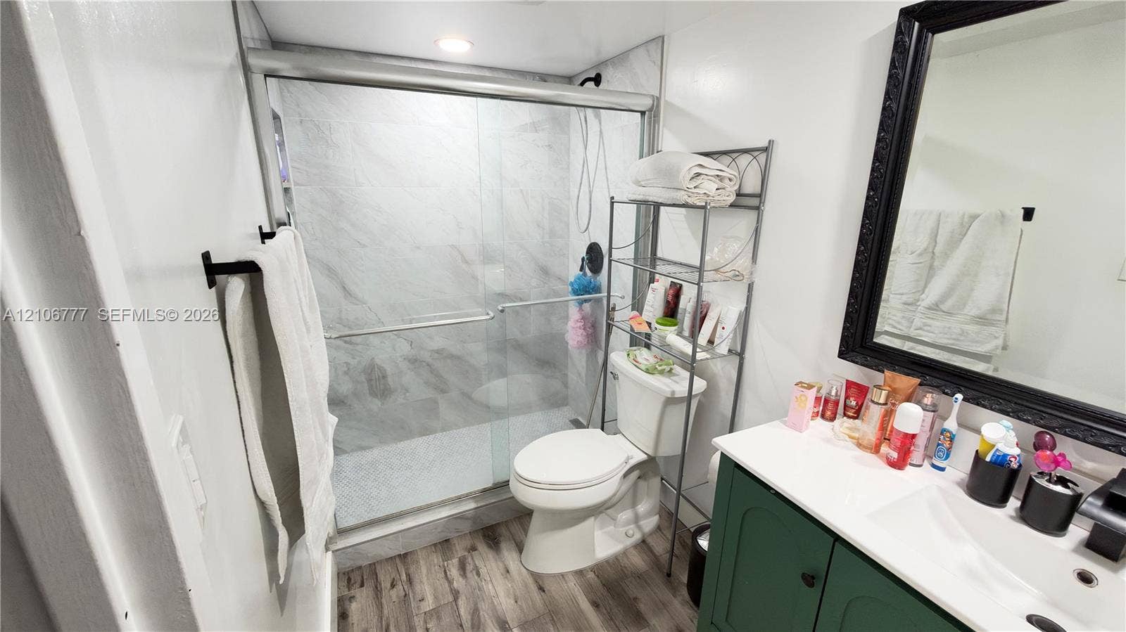1810 SW 81st Avenue, #2200, North Lauderdale, North Lauderdale, FL 33068 Bathroom featuring wood-finish flooring, a vanity with a white countertop and rectangular sink, a glass-enclosed shower with tiled walls, and a black-framed wall mirror