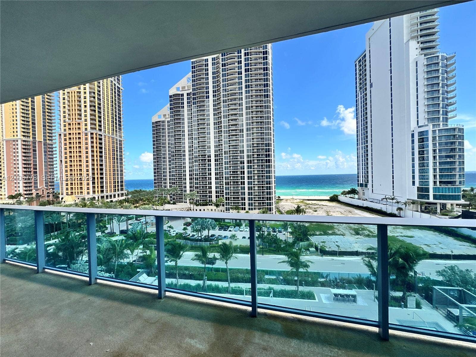 17550 Collins Avenue, #803, Sunny Isles Beach, Sunny Isles Beach, FL 33160 Balcony with transparent glass railing, offering ocean scenery, urban high-rise buildings, and palm trees