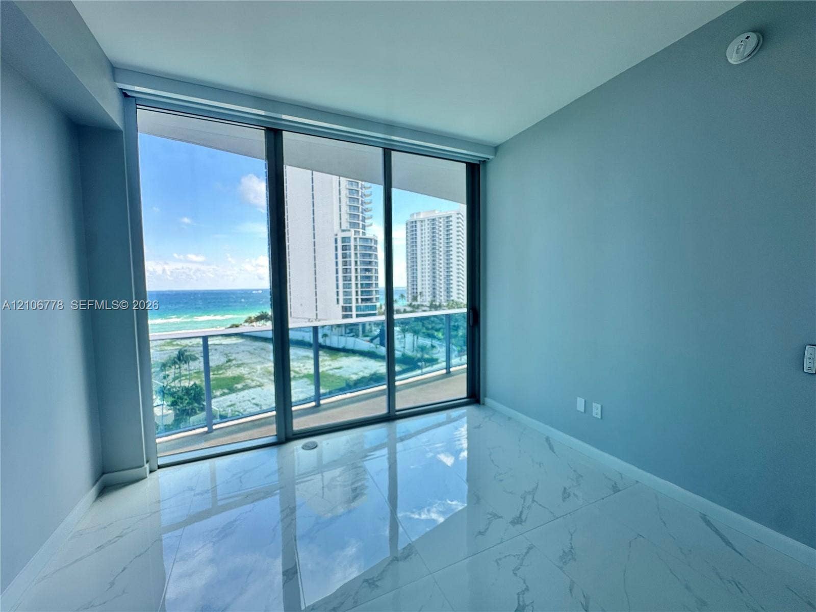 17550 Collins Avenue, #803, Sunny Isles Beach, Sunny Isles Beach, FL 33160 Floor-to-ceiling sliding glass doors, polished stone-finish tile flooring, and a glass-paneled balcony railing overlooking the ocean