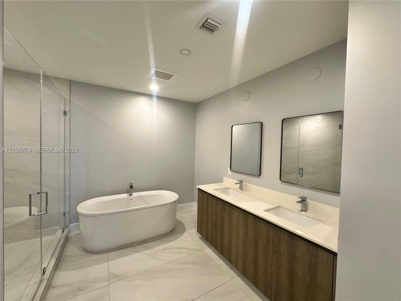 17550 Collins Avenue, #803, Sunny Isles Beach, Sunny Isles Beach, FL 33160 Dual-sink vanity with wood-finish cabinetry, quartz countertop, freestanding soaking tub, and glass-enclosed walk-in shower with tile surround