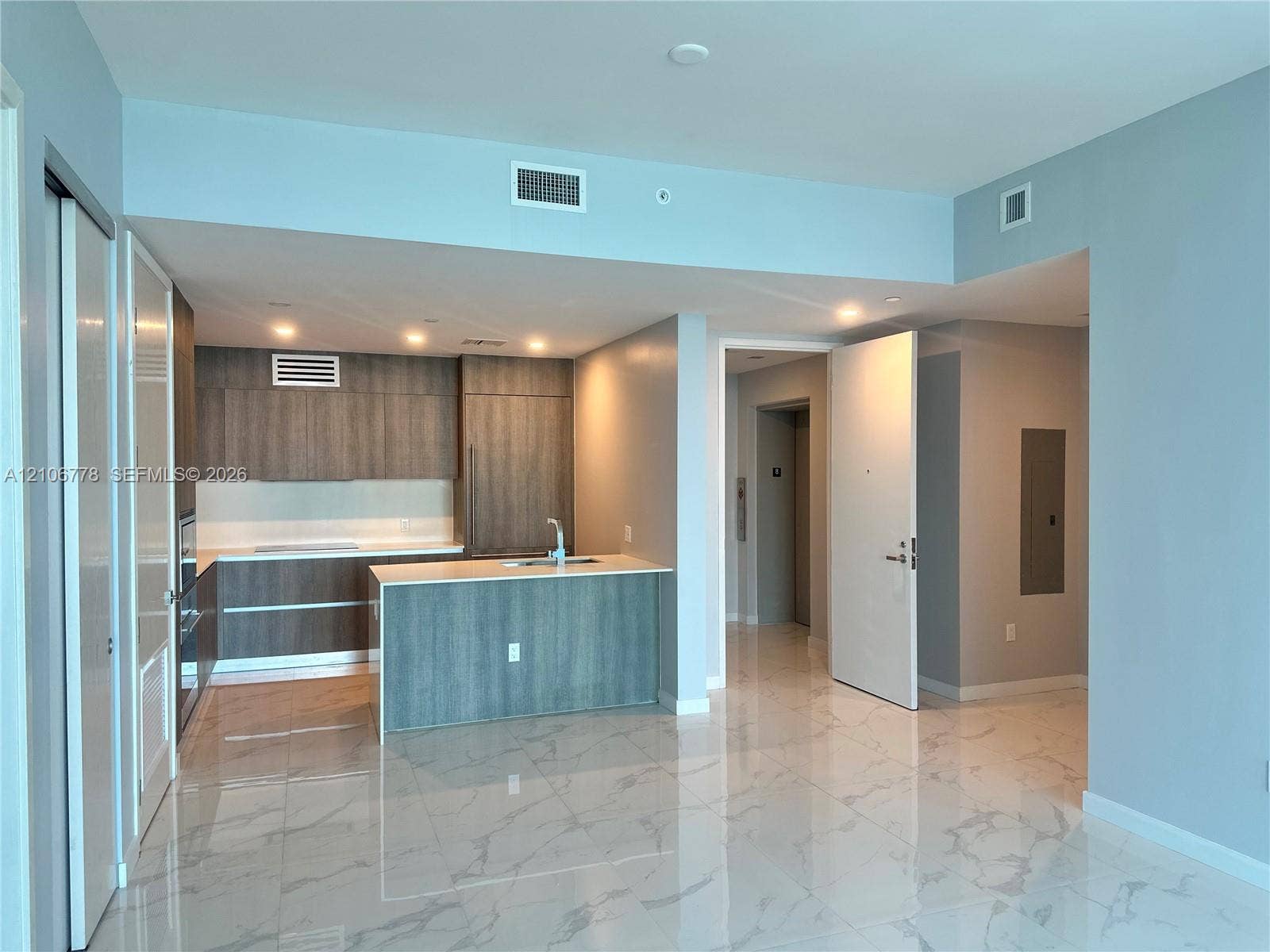 17550 Collins Avenue, #803, Sunny Isles Beach, Sunny Isles Beach, FL 33160 Modern open-concept living area featuring polished stone flooring, a central kitchen island with wood-finish cabinetry, stainless steel appliances, recessed ceiling lighting, and abundant natural light from expansive glass sliding doors