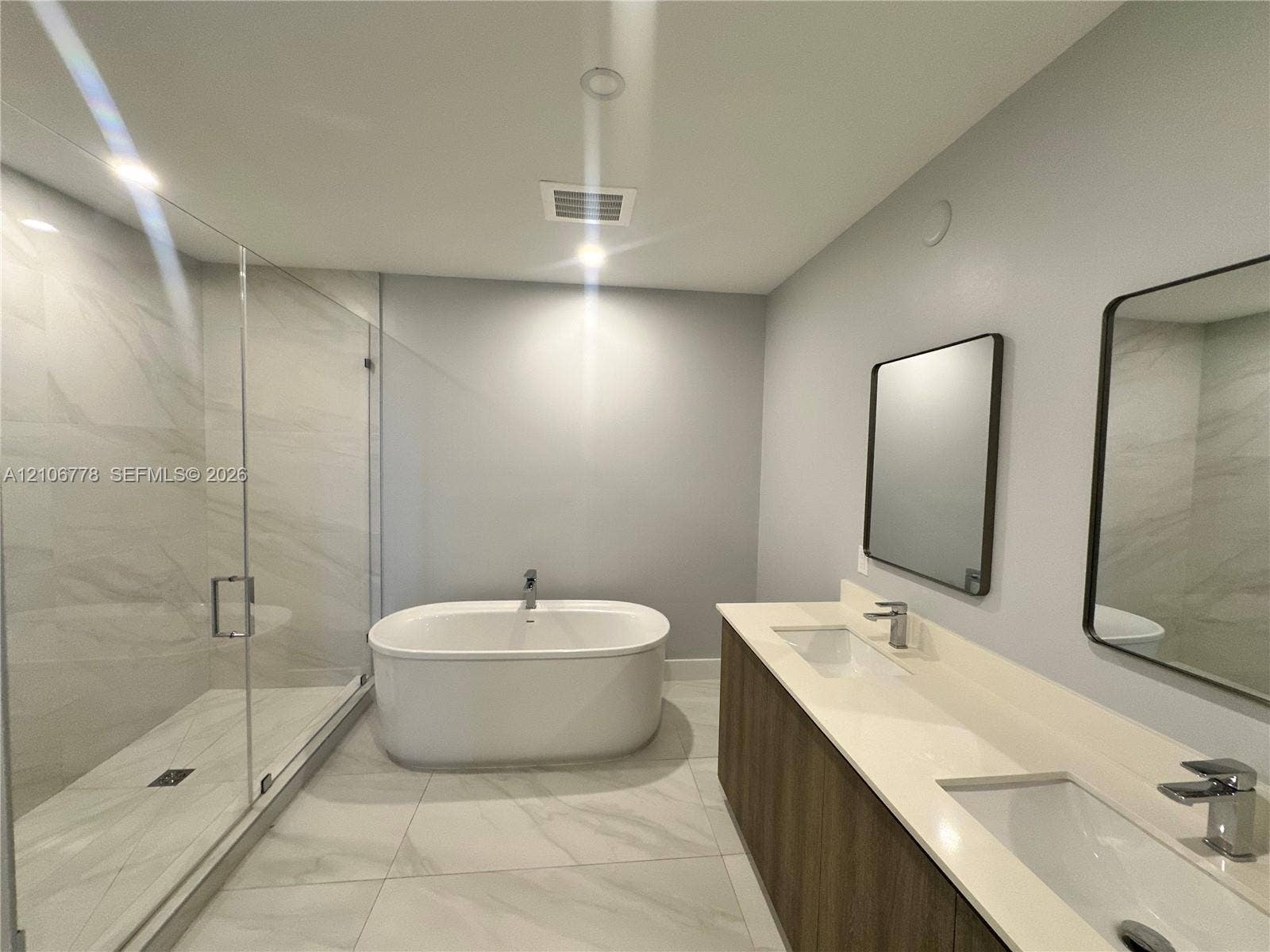 17550 Collins Avenue, #803, Sunny Isles Beach, Sunny Isles Beach, FL 33160 Double vanity with a composite countertop, wood-finish cabinetry, frameless walk-in glass shower, and freestanding soaking tub featuring large-format tile flooring