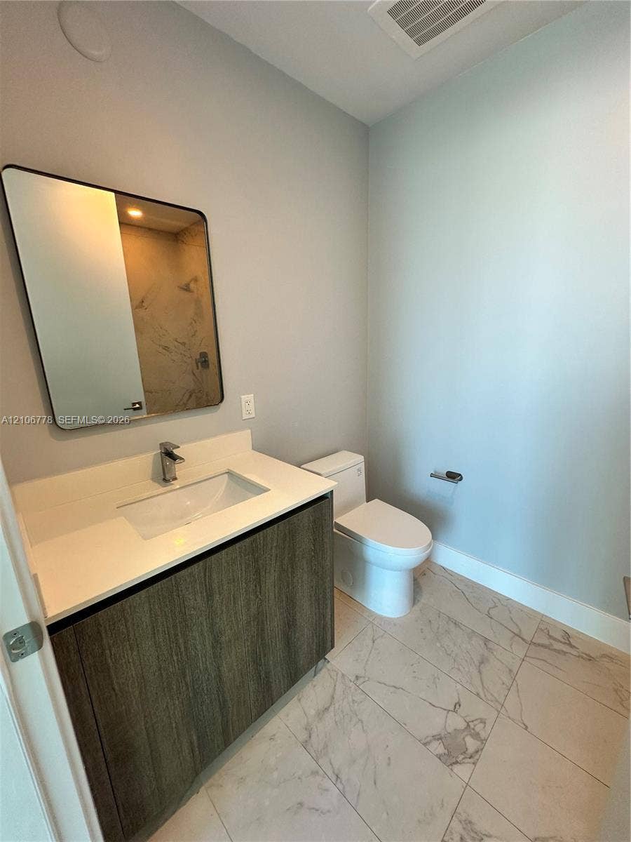 17550 Collins Avenue, #803, Sunny Isles Beach, Sunny Isles Beach, FL 33160 Modern vanity with a rectangular sink, stone-finish countertop, and wood-texture cabinetry, complemented by large-format tile flooring and a wall-mounted mirror with a black frame