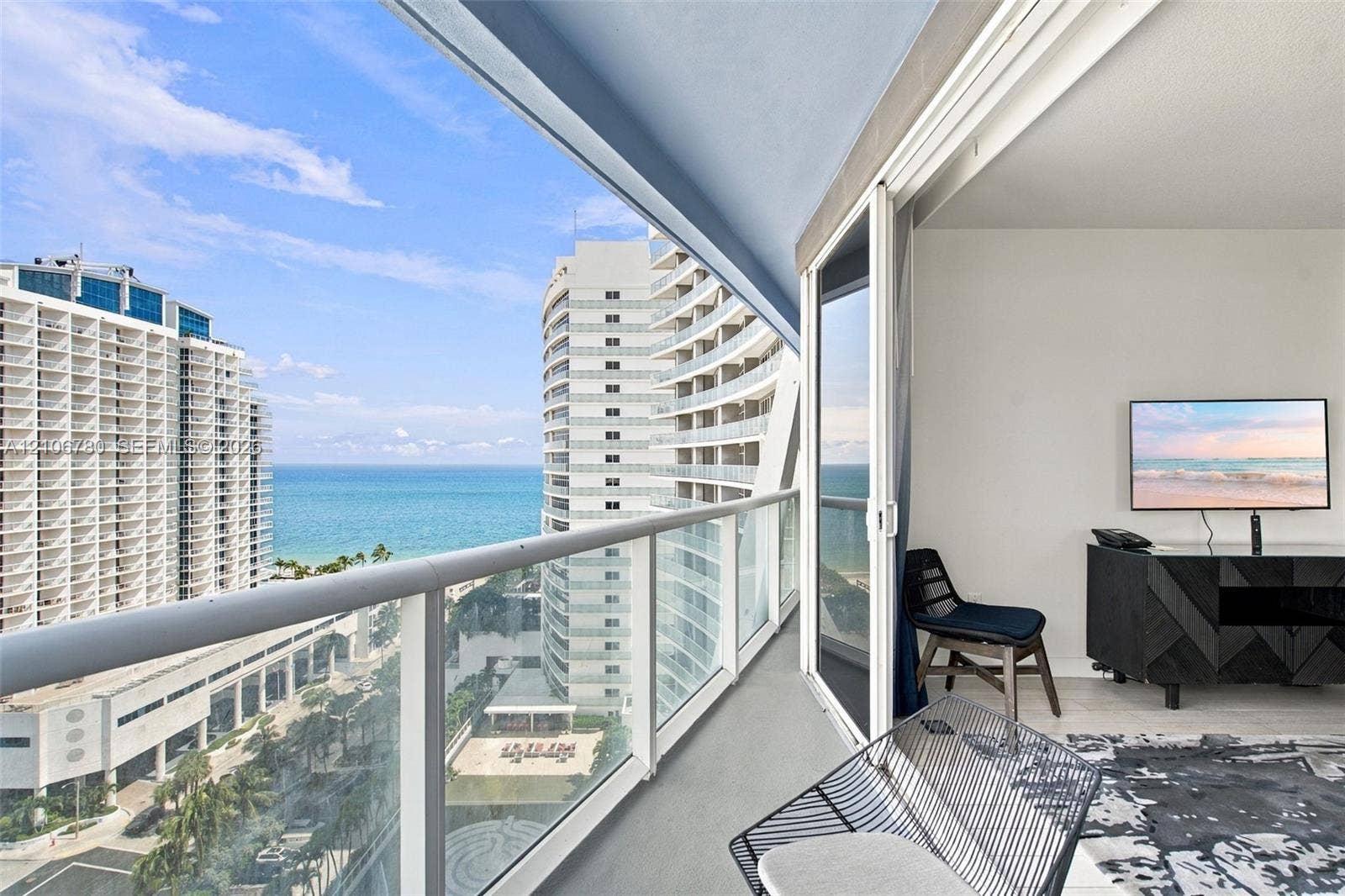 Private balcony featuring a glass-panel railing, sliding glass doors, and panoramic ocean and urban scenery