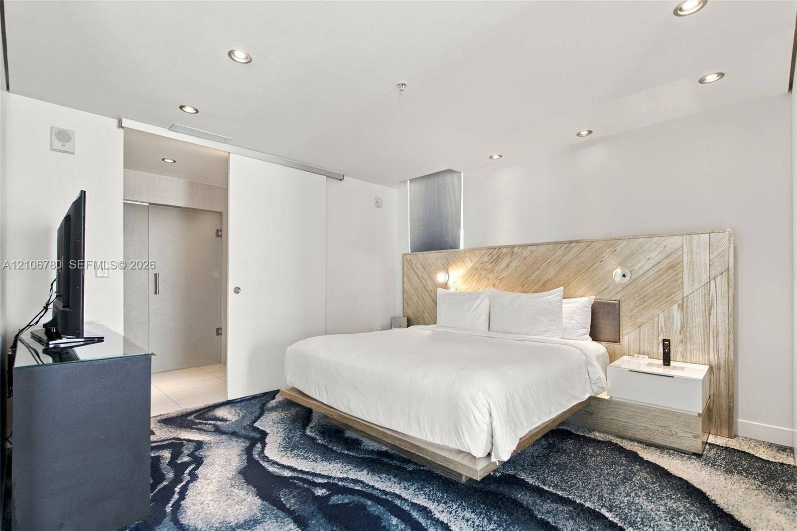 Recessed ceiling lighting, wood-paneled feature wall, floating platform base, and sliding interior door
