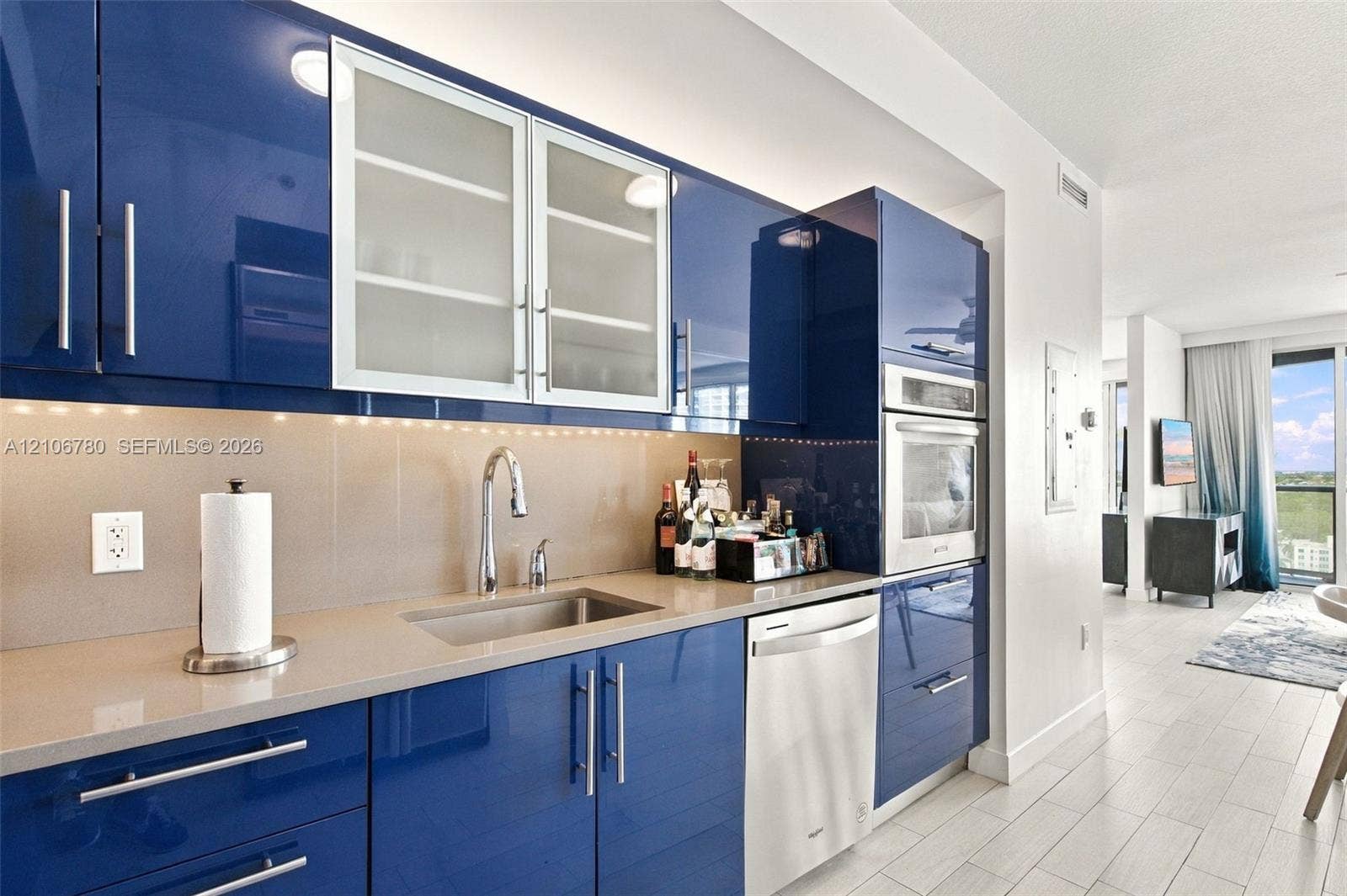 Modern kitchen featuring high-gloss blue cabinetry, stone-finish countertops, glass-panel upper cabinet doors, stainless steel built-in oven, and a stainless steel undermount sink
