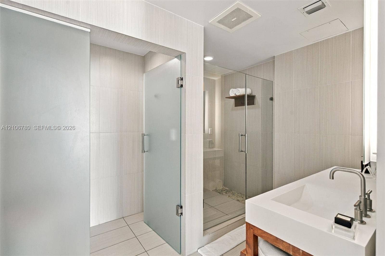 Custom vanity featuring a thick countertop and integrated rectangular sink, paired with a glass-enclosed shower with tiled walls and stone flooring, accented by frosted glass door panels and minimalist hardware