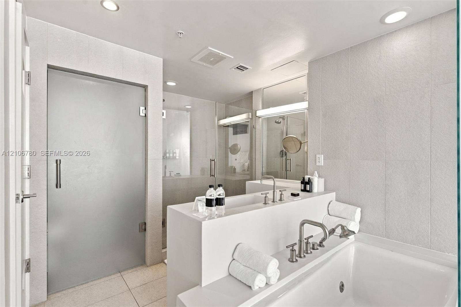 Bathroom featuring a deep soaking tub, polished nickel deck-mounted faucet, custom solid-surface vanity, walk-in glass-enclosed shower, and floor-to-ceiling tile surrounds