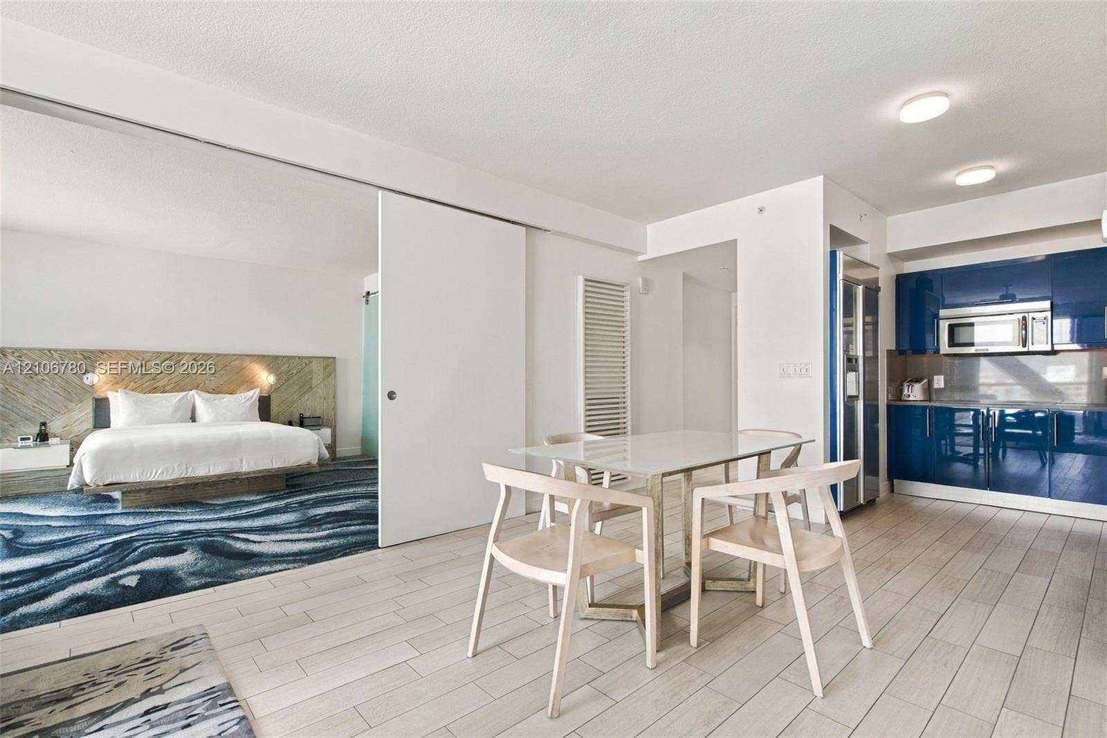 Open-concept living space featuring high-gloss blue cabinetry, built-in stainless steel appliances, light wood-finish flooring, and a large sliding door partition with stone-accented wall detailing