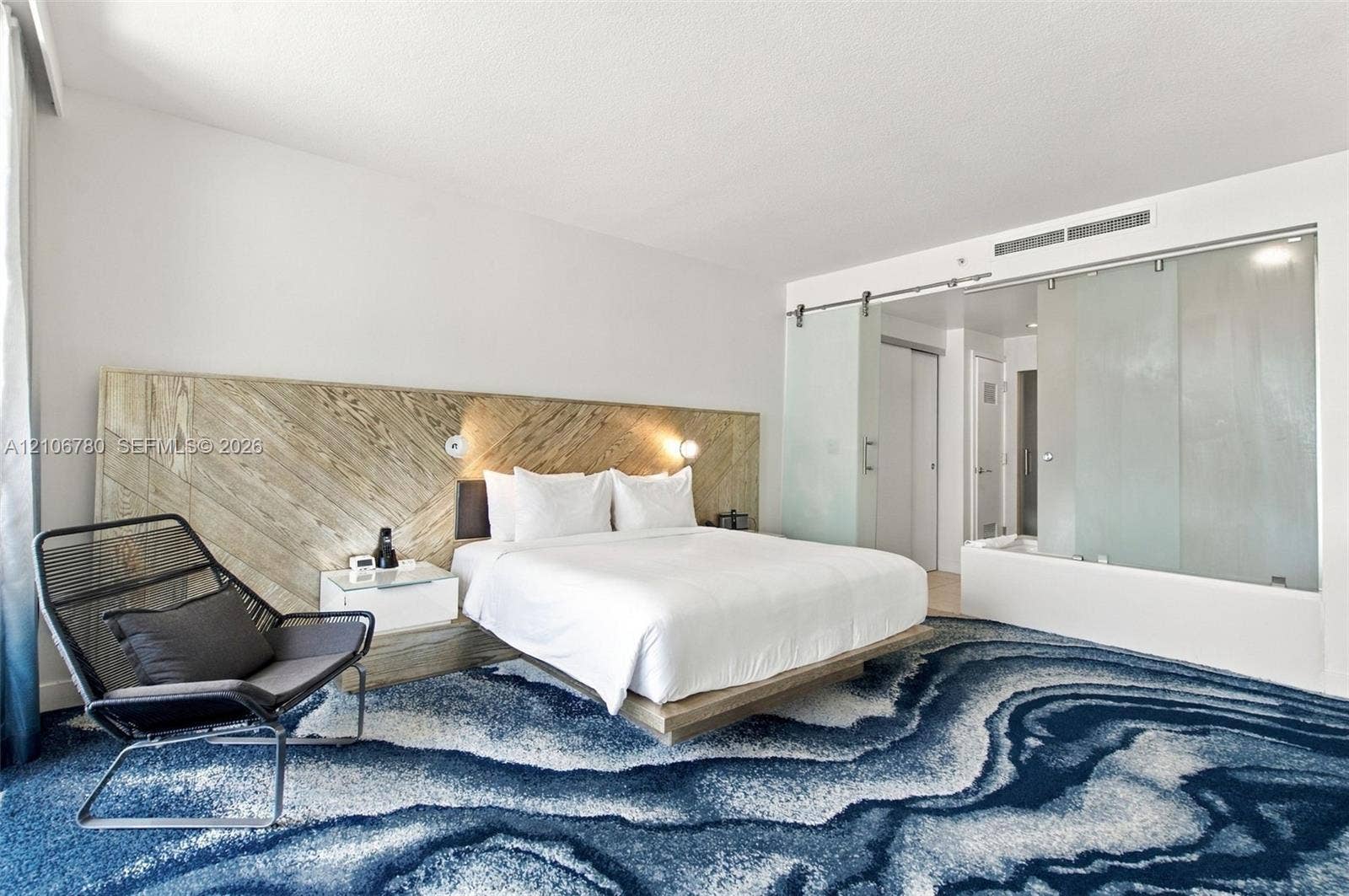 Custom built-in headboard featuring diagonal wood-finish detailing, platform bed frame, sliding frosted glass privacy panels with brushed metal hardware, and patterned wall-to-wall carpeting