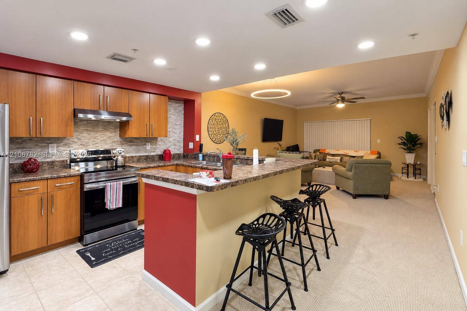 Kitchen featuring wood-finish cabinetry, stone-patterned countertops, a tiled backsplash, built-in stainless steel appliances, and a peninsula breakfast bar