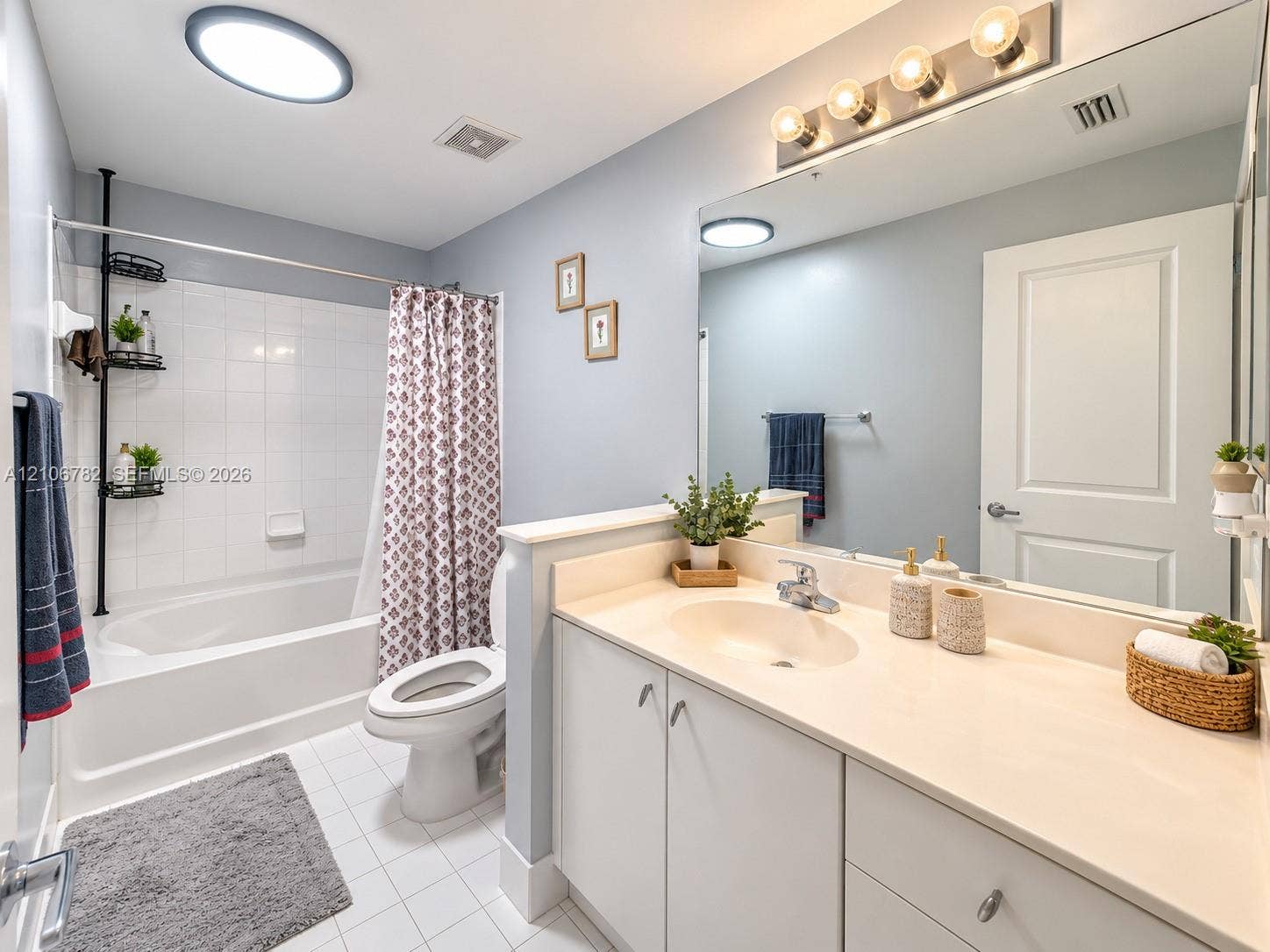 Bathroom featuring a tub-shower combination with white tile surround, vanity with an integrated sink, neutral countertop, expansive wall-mounted mirror, and overhead lighting