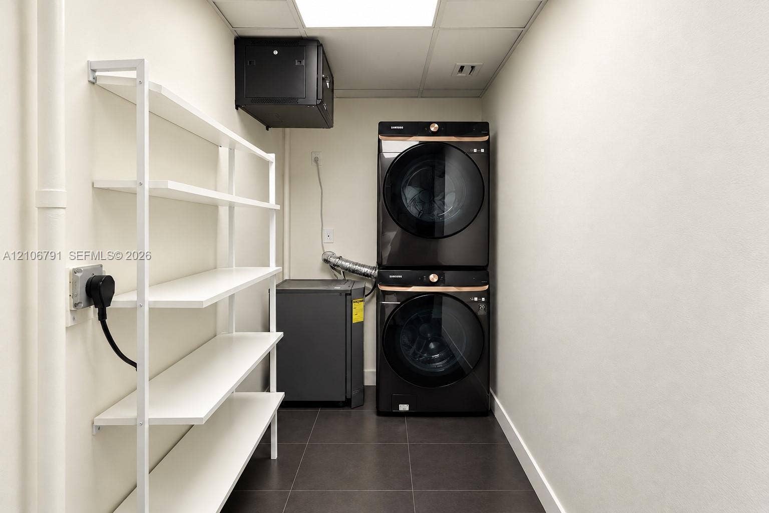 1684 SE 10th Avenue, Fort Lauderdale, Fort Lauderdale, FL 33316 Laundry area featuring large-format dark tile flooring, built-in open white shelving, and a stacked washer and dryer set