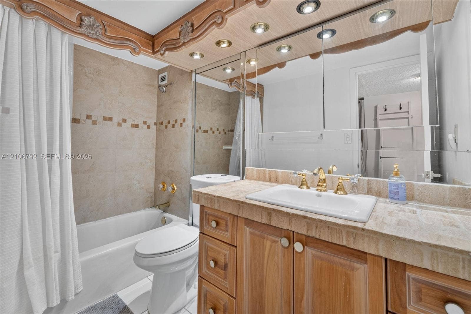 2030 S Ocean Drive, #723, Hallandale Beach, FL 33009 Bathroom featuring a vanity with a stone countertop, inset sink, brass-finish faucet, custom wood cabinetry, and recessed lighting integrated into a decorative wood-trimmed mirror surround, with stone-tile tub surround and decorative mosaic inlay