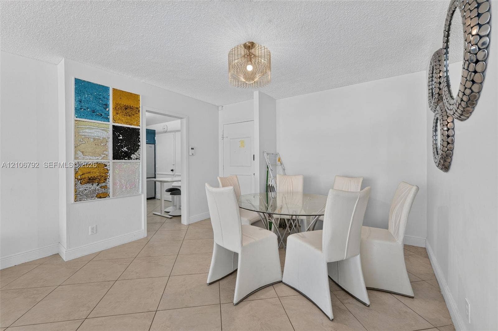 2030 S Ocean Drive, #723, Hallandale Beach, FL 33009 Interior space featuring neutral tile flooring, a tiered metal chandelier, and a decorative wall accent composed of multi-colored textured panels