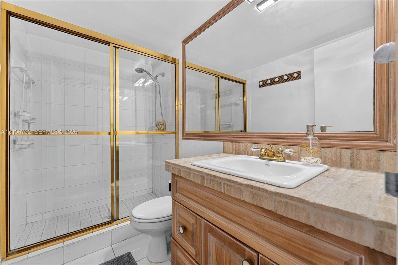 2030 S Ocean Drive, #723, Hallandale Beach, FL 33009 Bathroom featuring a vanity with a stone countertop, an integrated sink with gold-tone hardware, a large framed mirror, and a walk-in shower with gold-tone sliding doors and white wall tile