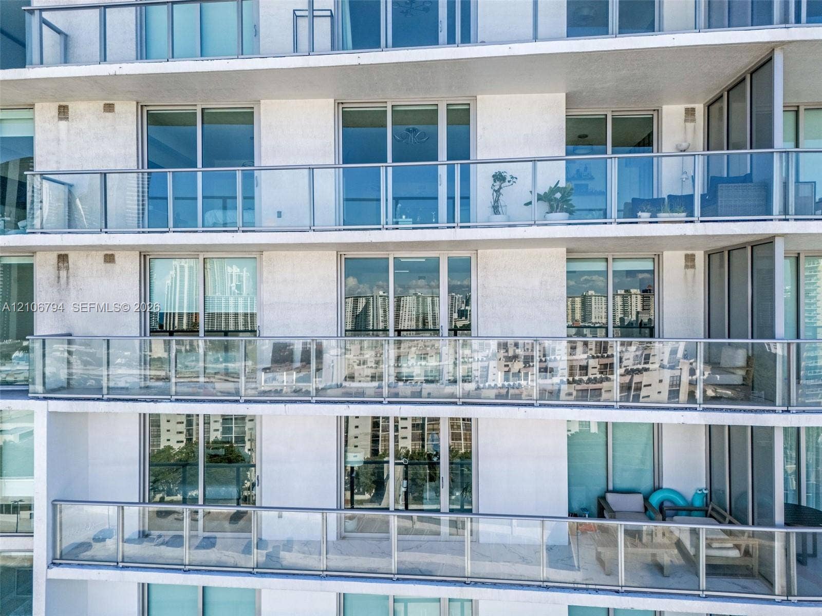 High-rise building exterior featuring private glass-railed balconies and floor-to-ceiling sliding glass doors