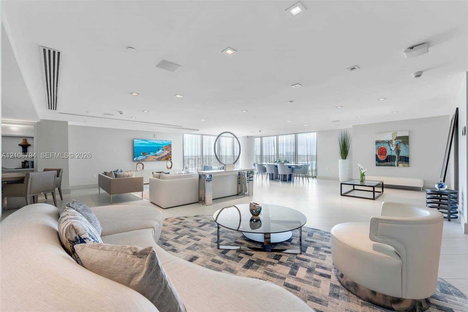 Open-concept interior featuring floor-to-ceiling windows, neutral tile flooring, recessed ceiling lighting, and built-in display shelving