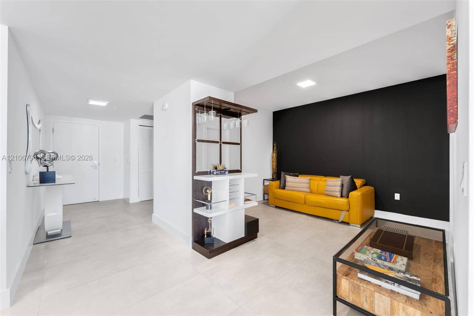 Open floor plan featuring large-format tile flooring, a custom built-in beverage service unit, recessed lighting, and a dramatic high-contrast accent wall