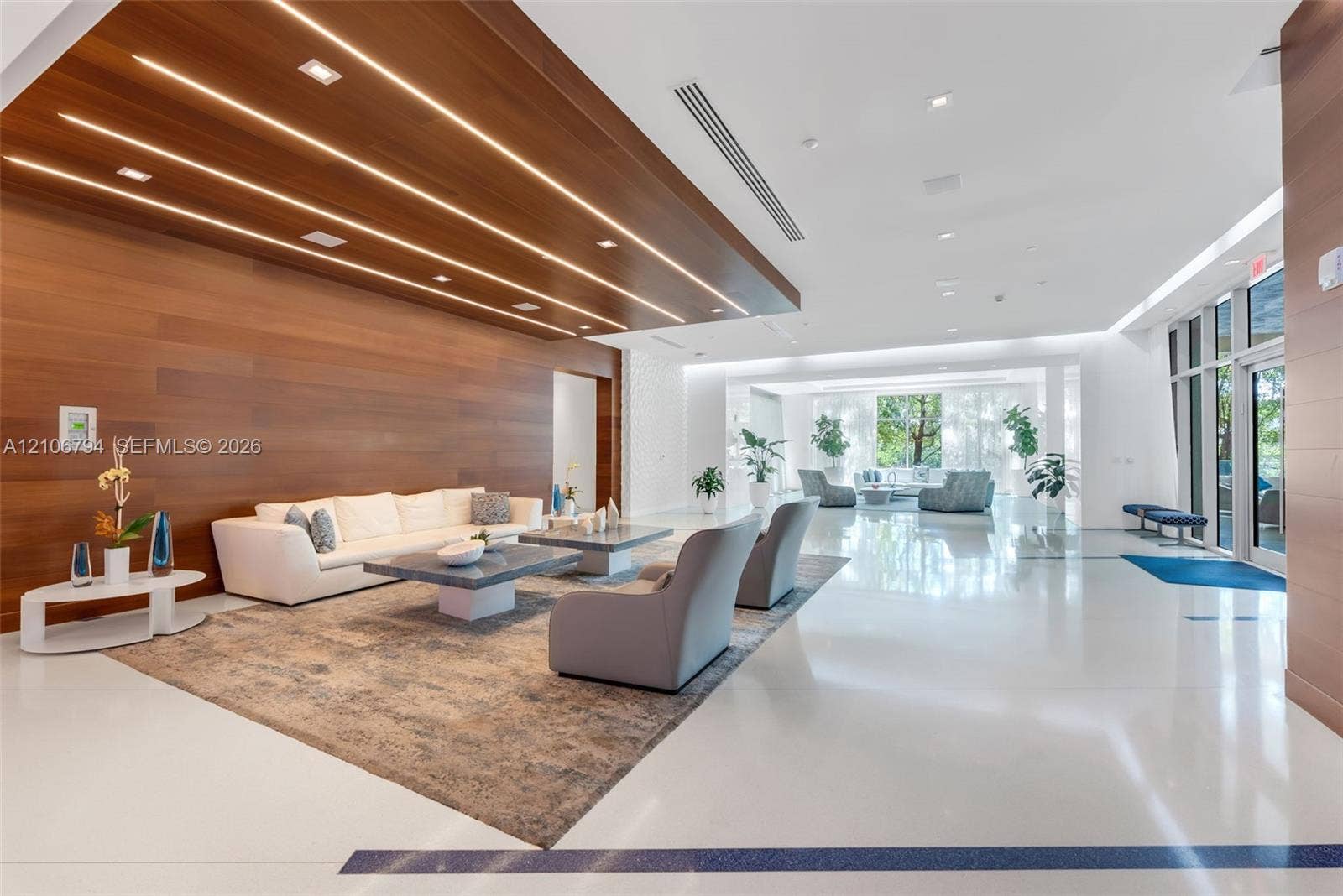 Large common area featuring high-gloss flooring, wood-paneled accent wall, recessed linear lighting, and floor-to-ceiling glass windows