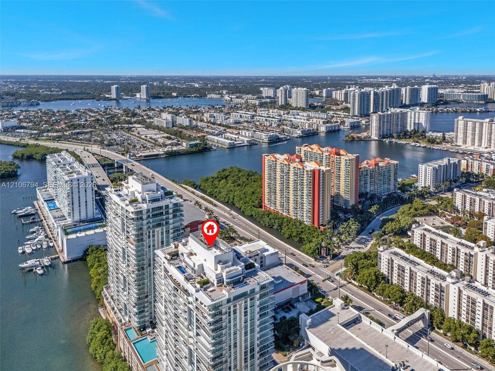 Aerial perspective of high-rise building with balcony terraces, situated along a coastal waterway featuring marina boat slips and expansive water frontage