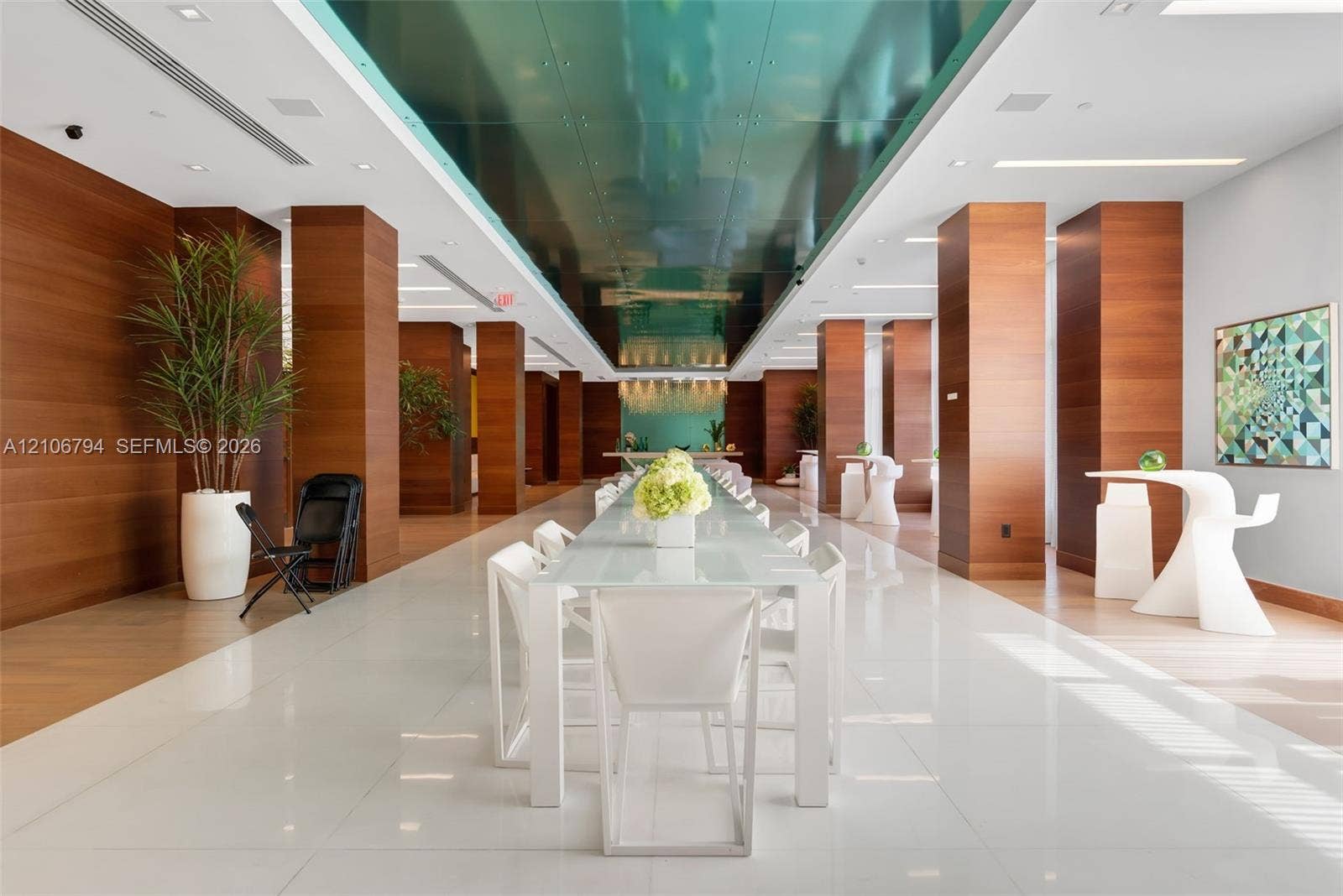Spacious interior featuring floor-to-ceiling wood-paneled columns, polished white tile flooring, a glossy teal recessed ceiling feature, and integrated linear lighting