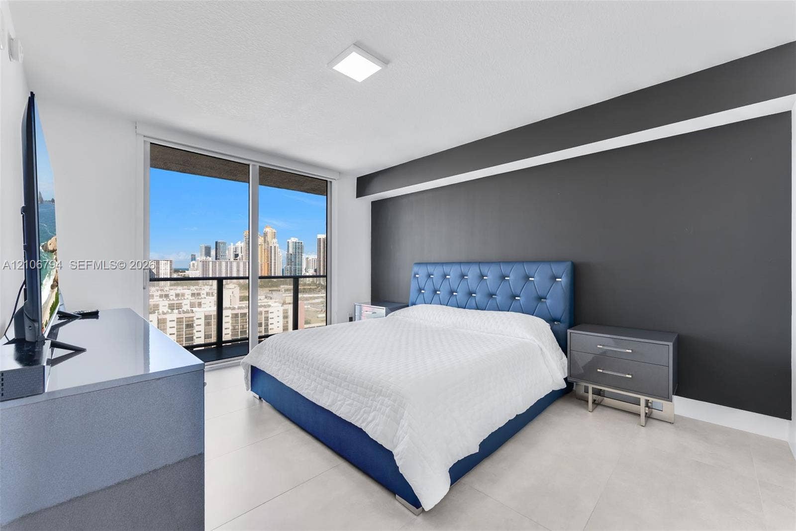 Large floor-to-ceiling glass sliding doors, dark charcoal accent wall, neutral oversized floor tile, and a private balcony featuring a metal railing