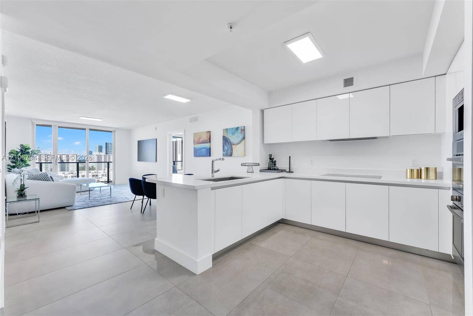 Kitchen featuring white high-gloss cabinetry, stone countertops, stainless steel appliances, and large-format tile flooring, complemented by floor-to-ceiling glass panel windows