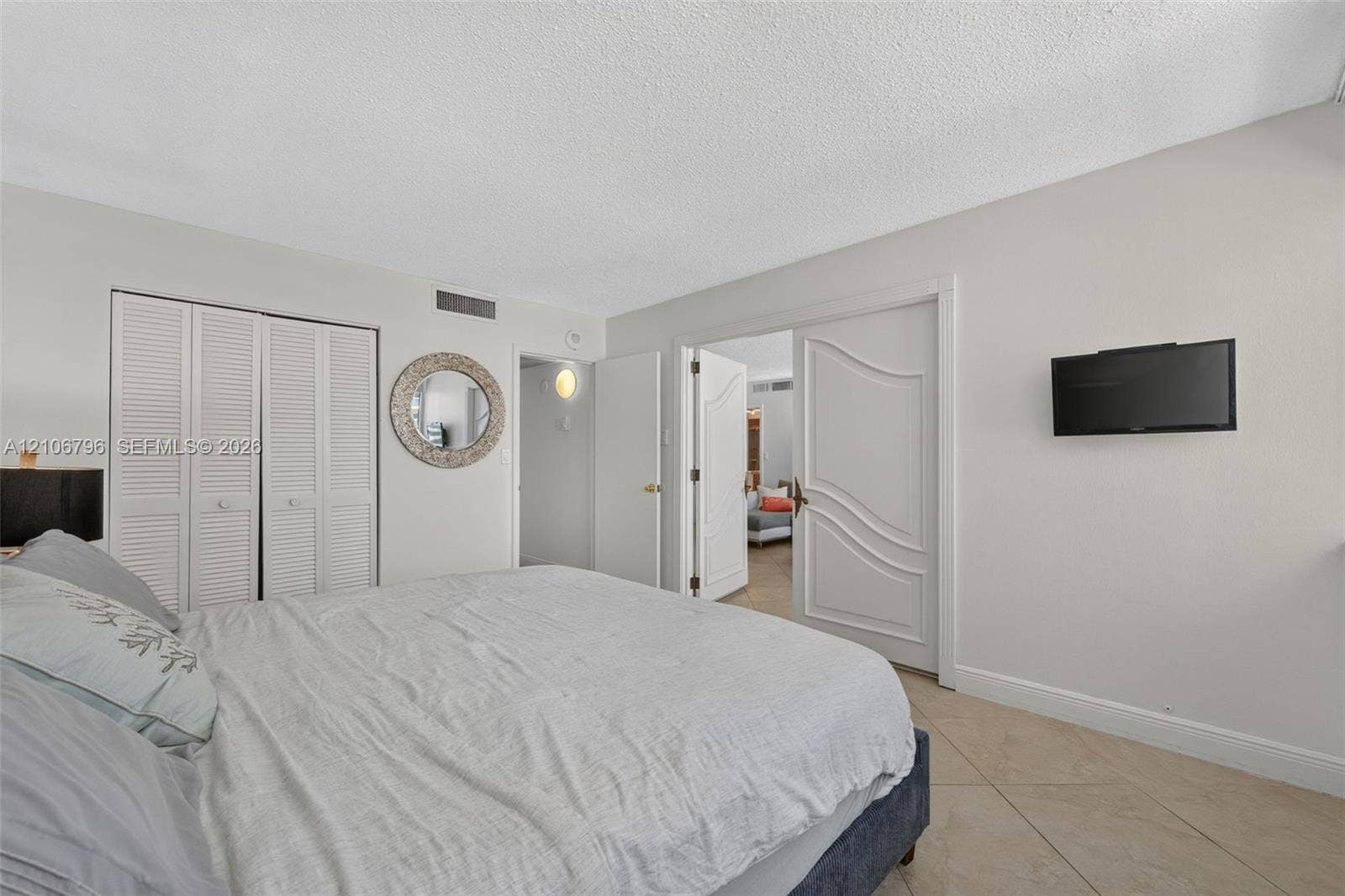 Neutral-toned interior featuring louvered closet doors, arched-panel dual doors, and neutral-toned tile flooring