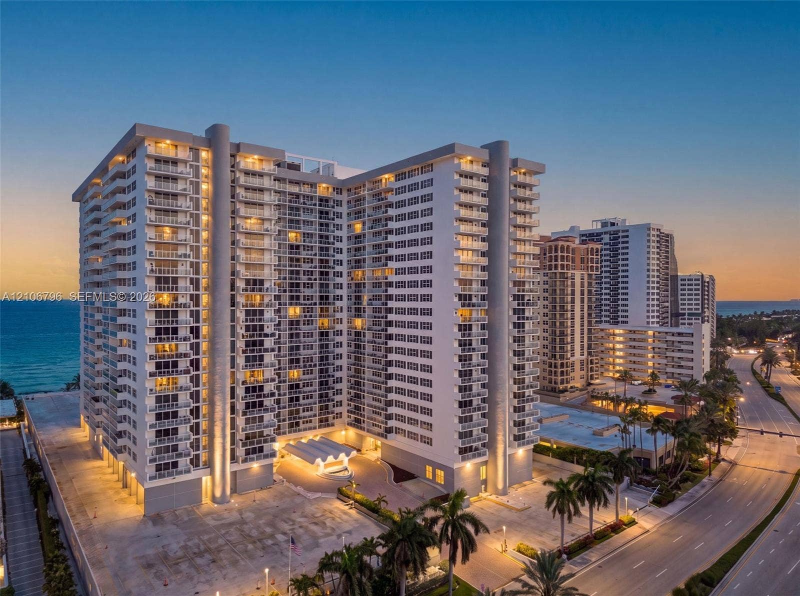 High-rise structure featuring stacked private balconies, a porte-cochere entrance, concrete construction, and direct coastal positioning