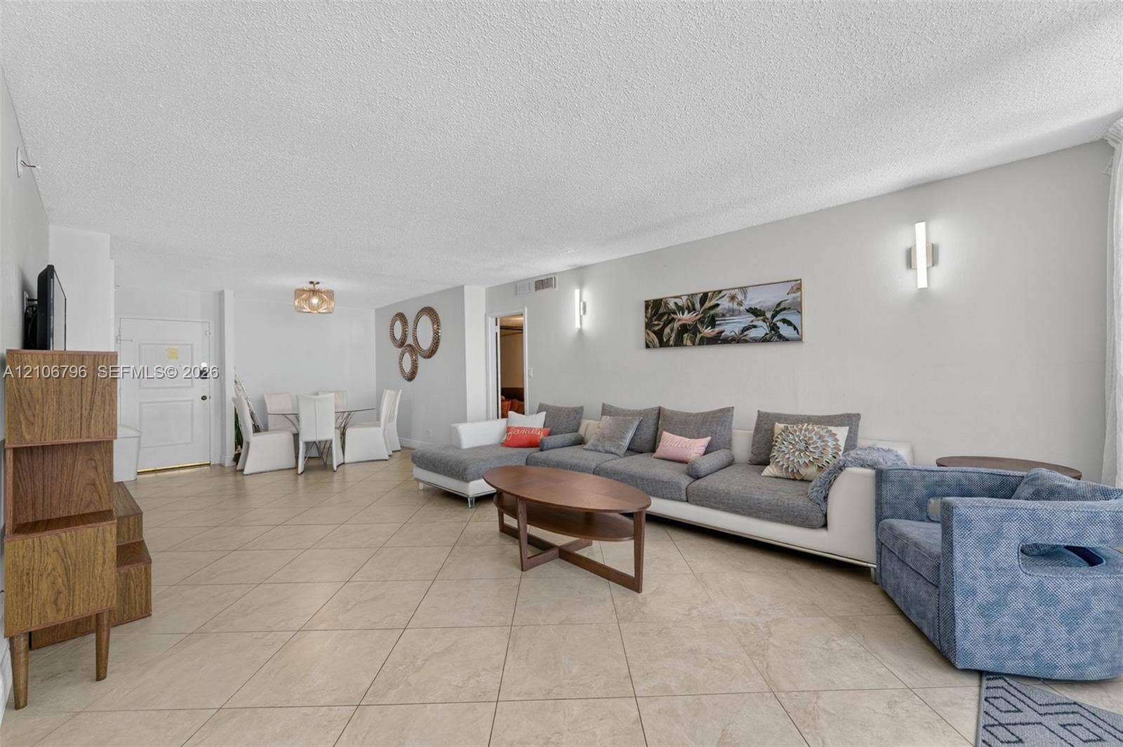Open floor plan featuring neutral large-format tile flooring, textured ceiling finish, and wall-mounted light fixtures